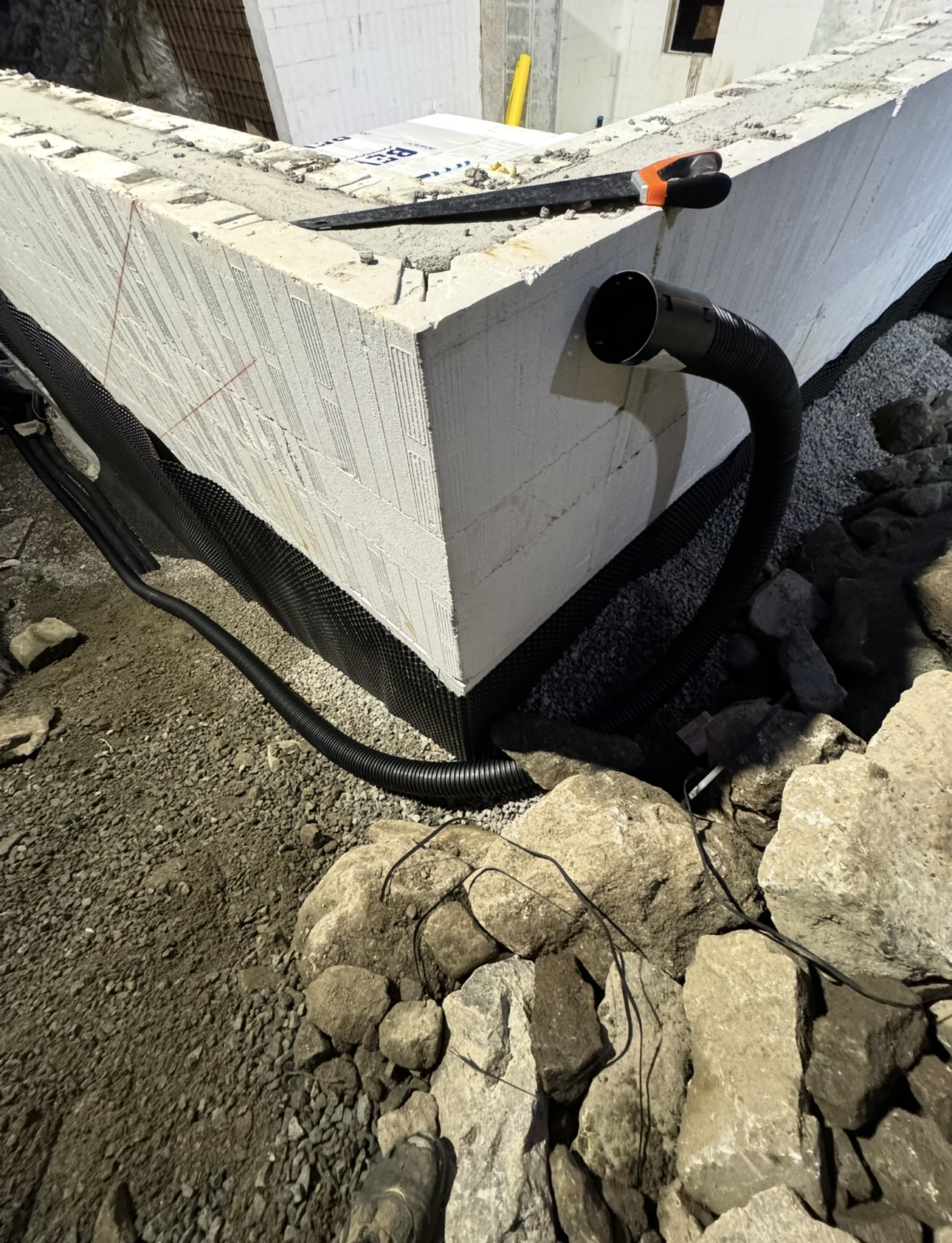 Hjørne av grunnmur med drensrør gjennom muren og knottplast